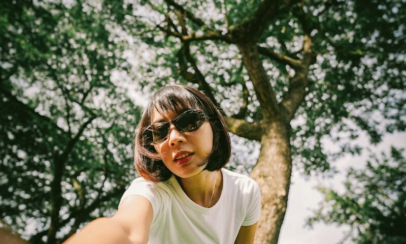 a woman standing next to a tree wearing sunglasses