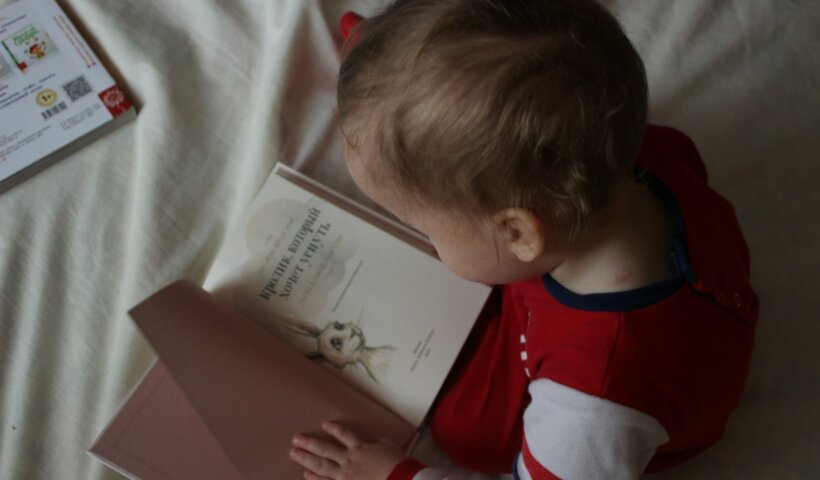 baby sitting on bed while reading on book